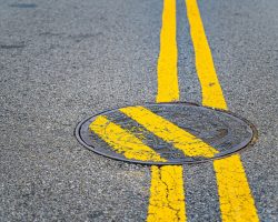 Double yellow lines painted over a manhole cover to humorous effect.